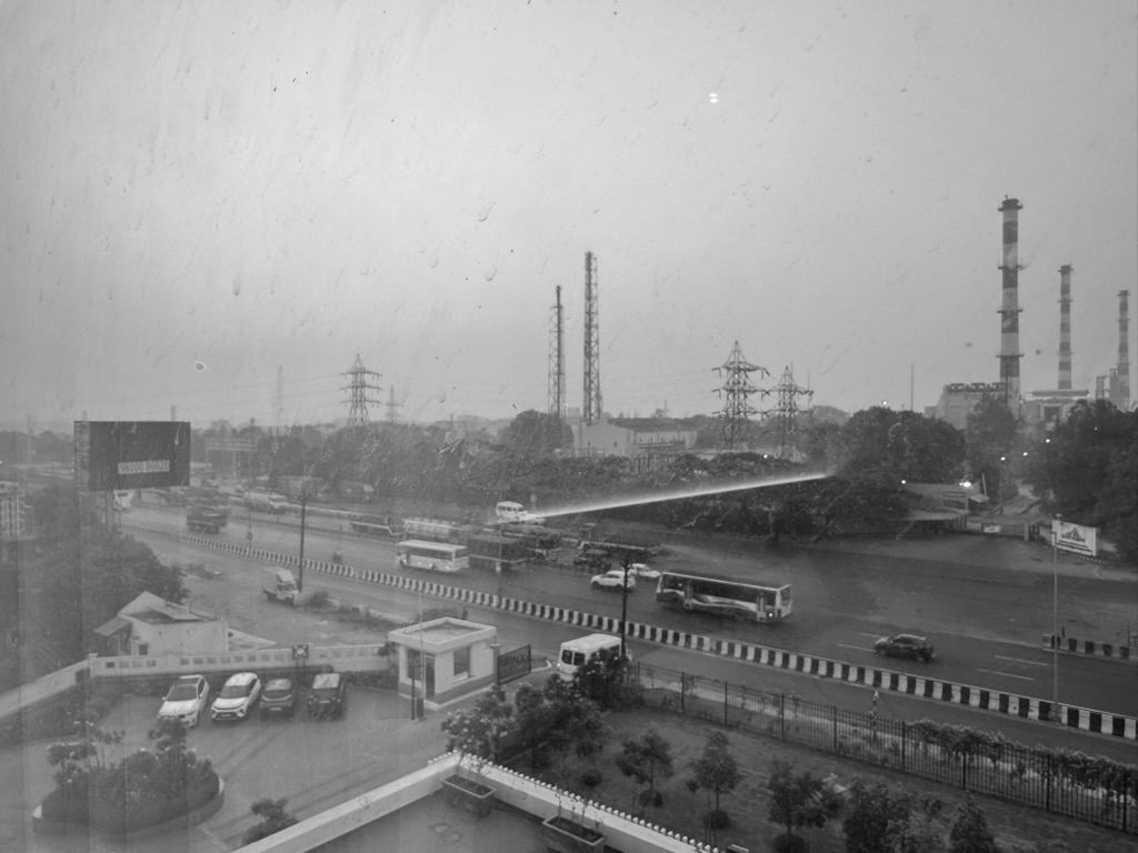 An industrial corridor at dawn, a multi-lane highway with buses and workers' transport, power-transmission towers and factory chimneys on the horizon