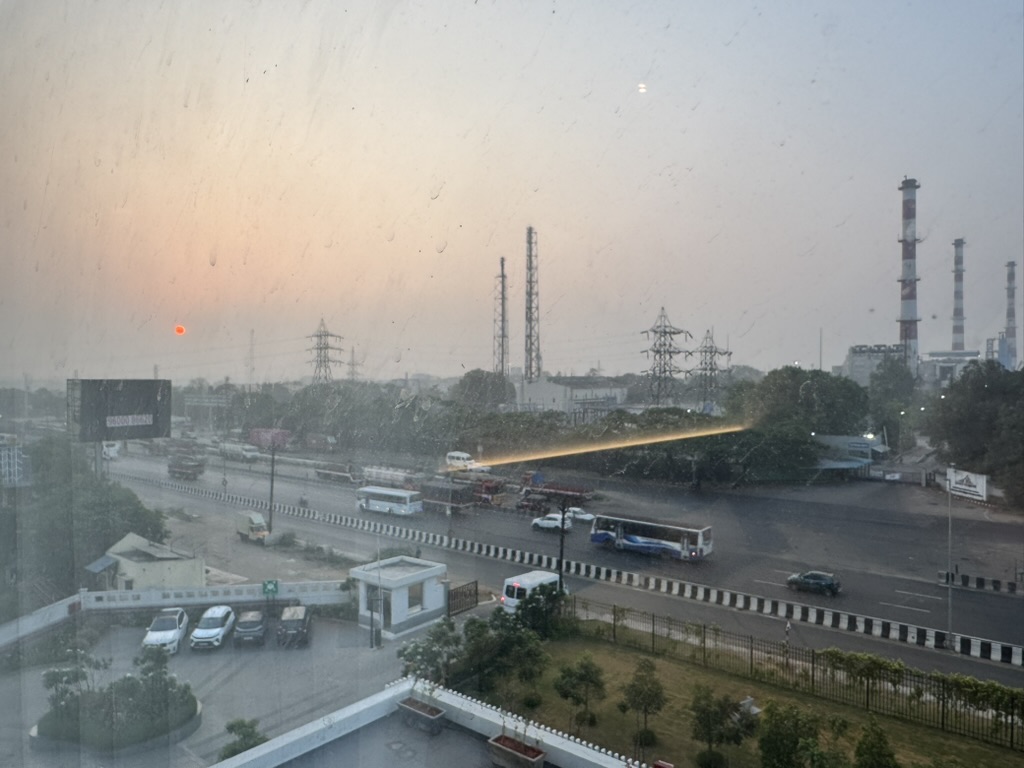 Wide operational view of an active petrochemical facility at daylight, with multiple smokestacks, cooling towers, logistics vehicles, and warehouse infrastructure showing the scale of industrial operations