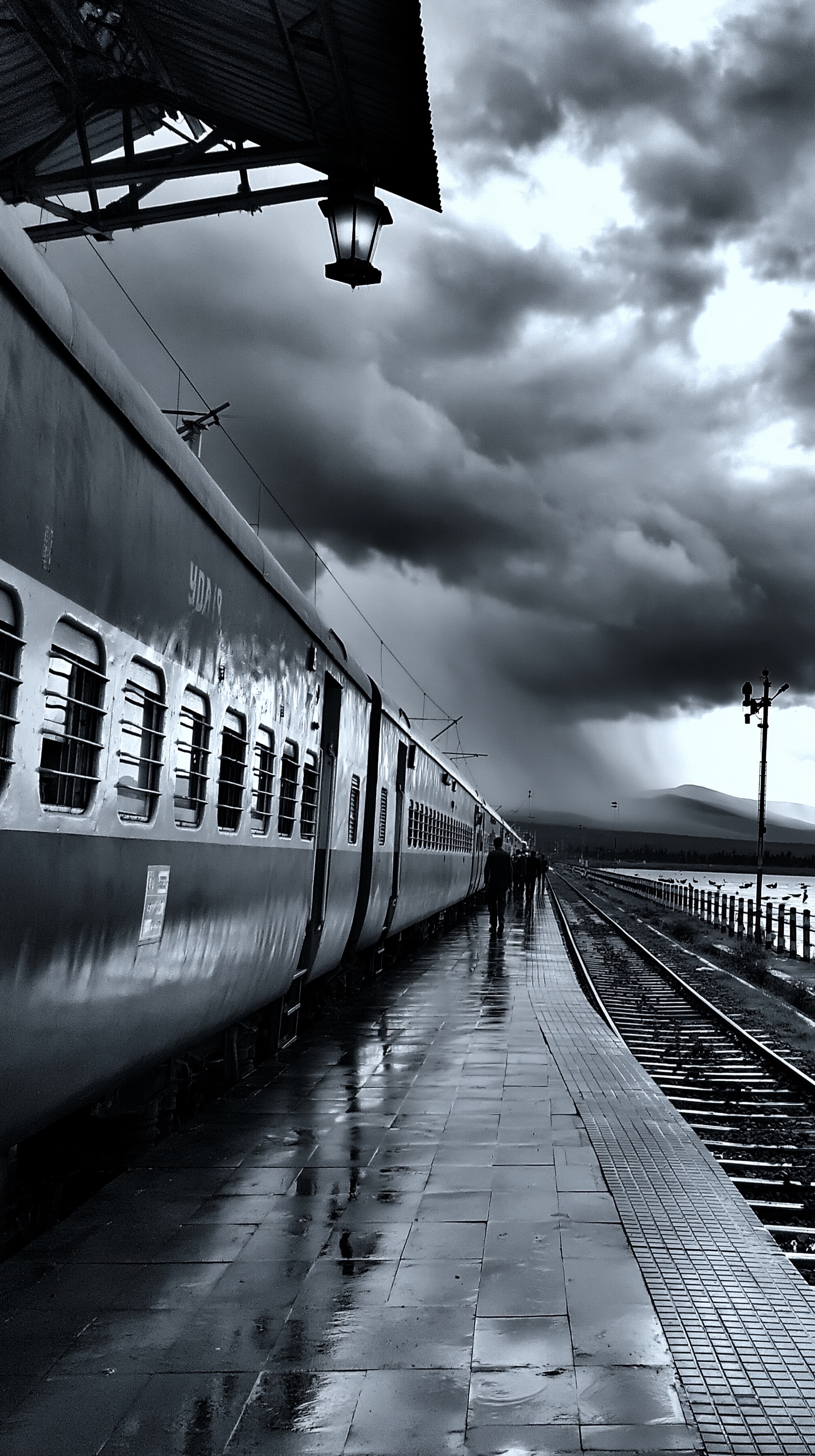 A passenger train beside a rain-soaked platform beneath monsoon clouds