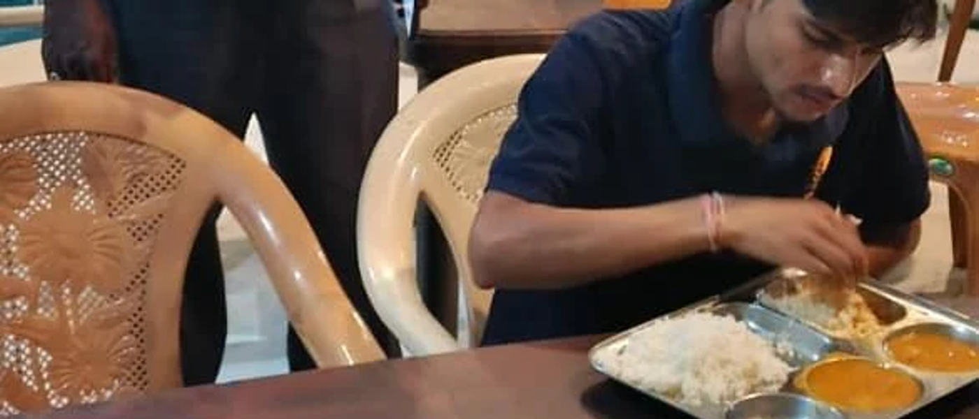 A member eating a home-style thali meal in the common dining area of a Nia Studio near a manufacturing plant