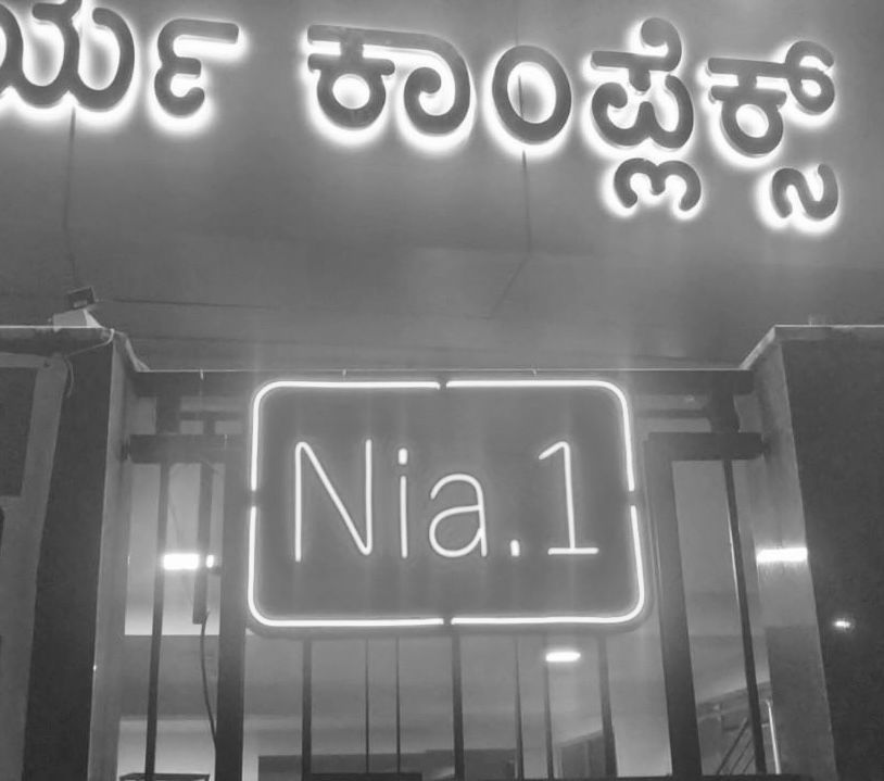An illuminated neon 'Nia.1' sign at the entrance of a Nia residence inside a commercial complex